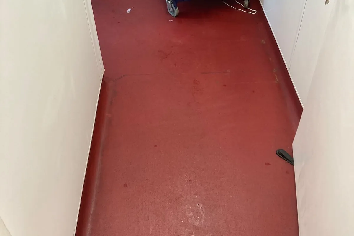 A red safety floor in a back-of-house corridor, dulled and marked before the clean