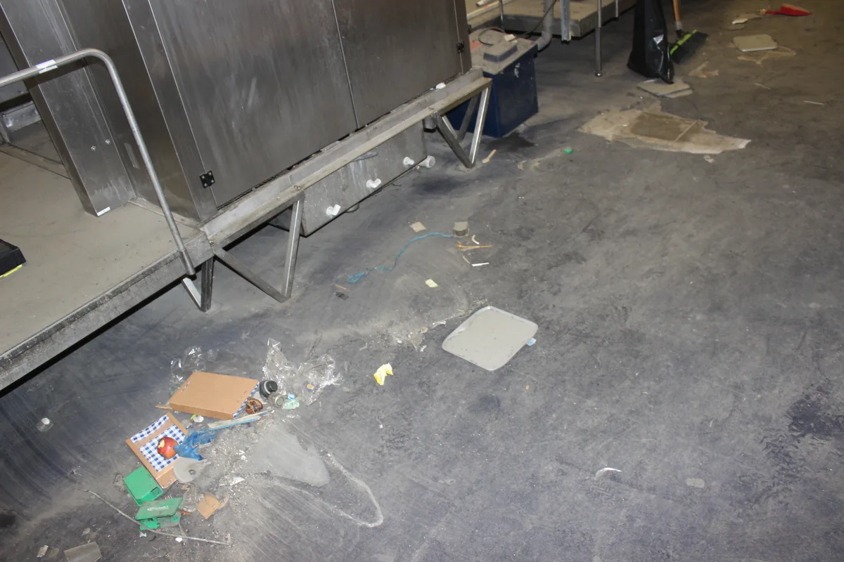 A floor under storage racking covered in litter and debris before the clean